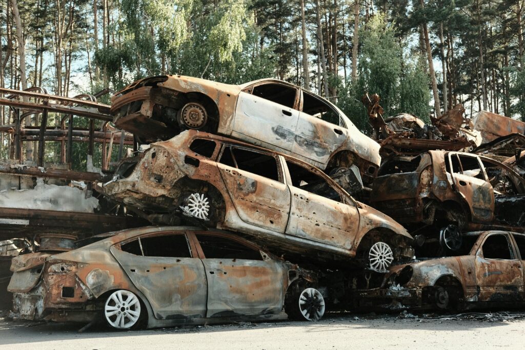 Pile of rusty destroyed cars in outdoor junkyard surrounded by trees.